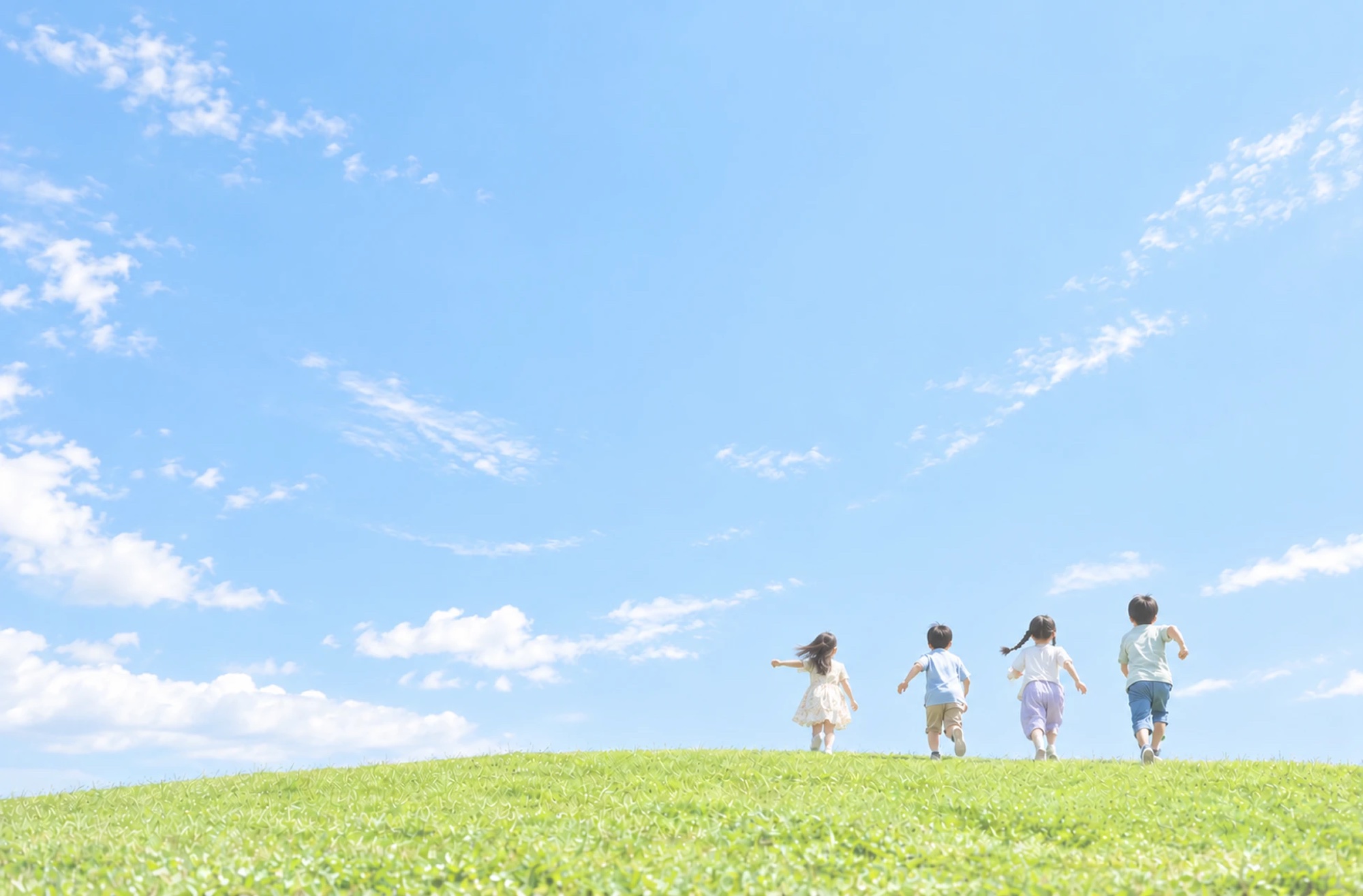 青空の下、草原を駆けていく子どもたち